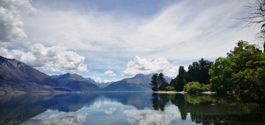 refelction of greenery and mountainous range on a calm lake wakatipu on sunny day